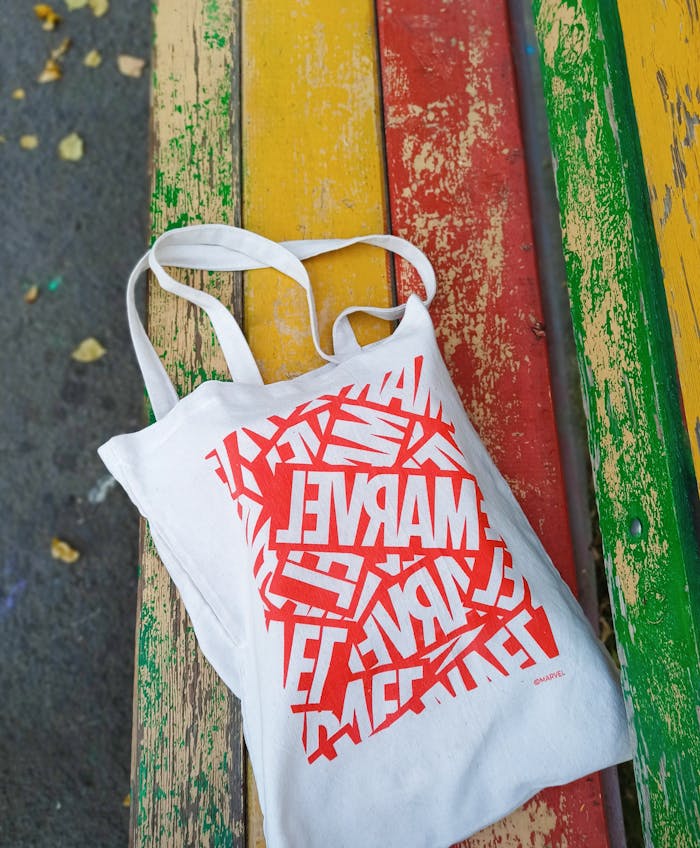 A canvas tote bag with Marvel design on a vibrant colored bench outdoors.